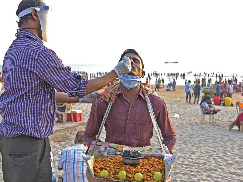 عامل صحي يجري فحص كورونا لبائع متجول على شاطئ مومباي أمس        (أ ف ب)