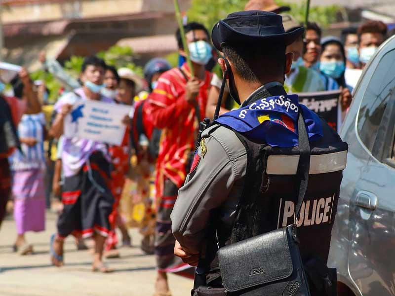 أحد قوات ميانمار يراقب محتجين مناهضين للانقلاب العسكري 