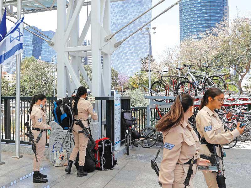 جنديات إسرائيليات أمام أعلام تم إنزالها إلى نصف الصاري في يوم الحداد بمدينة تل أبيب أمس (أ ف ب)n