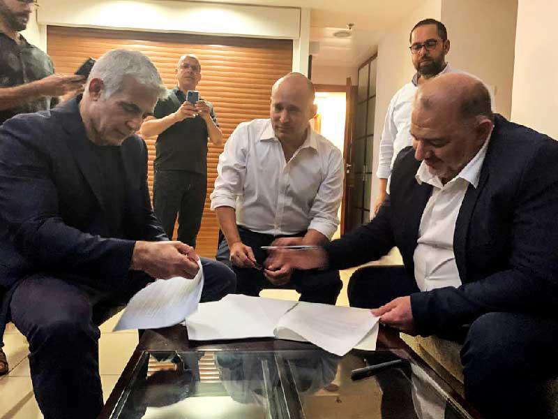 منصور عباس يوقع الاتفاق مع لابيد وبينيت في تل أبيب أمس الأول (رويترز)n