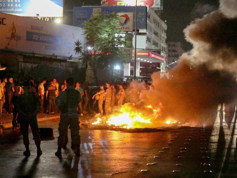 جنود الجيش اللبناني يقفون في حراسة مع تصاعد الدخان من الإطارات التي أضرمها المتظاهرون خلال احتجاج ، بعد أن قال مصرف لبنان المركزي إنه سيوقف عمليات السحب المصرفي من الحسابات الدولارية