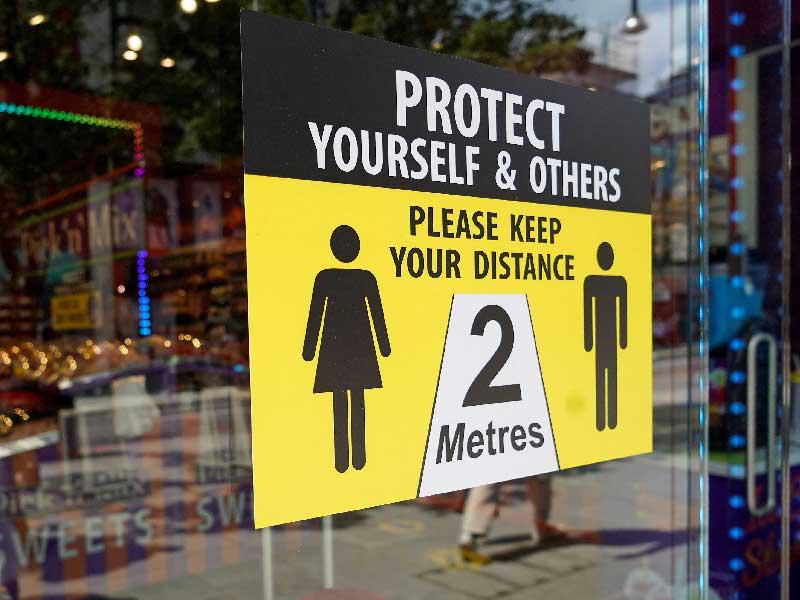 لافتة خارج متجر تطلب من العملاء المسافة الاجتماعية
