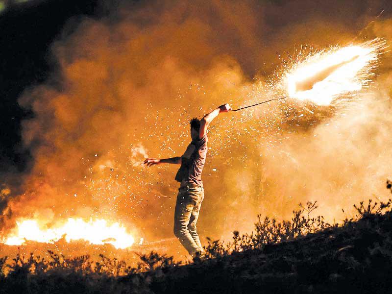 فلسطيني يرمي مواد مشتعلة باتجاه الشريط الحدودي بين إسرائيل وغزة أمس الأول (أ ف ب)