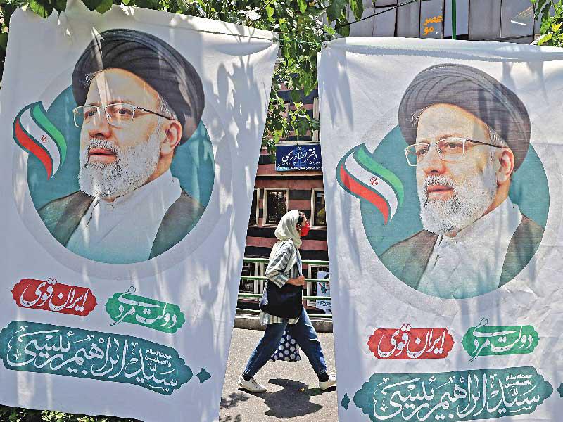 إيرانية تمر بين صورتين لرئيسي في طهران (أ ف ب) 