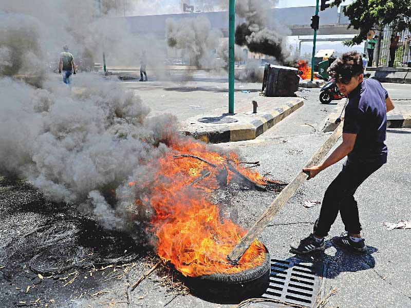 متظاهر لبناني يقفل الطريق بإطار مشتعل في بيروت أمس (أ ف ب)