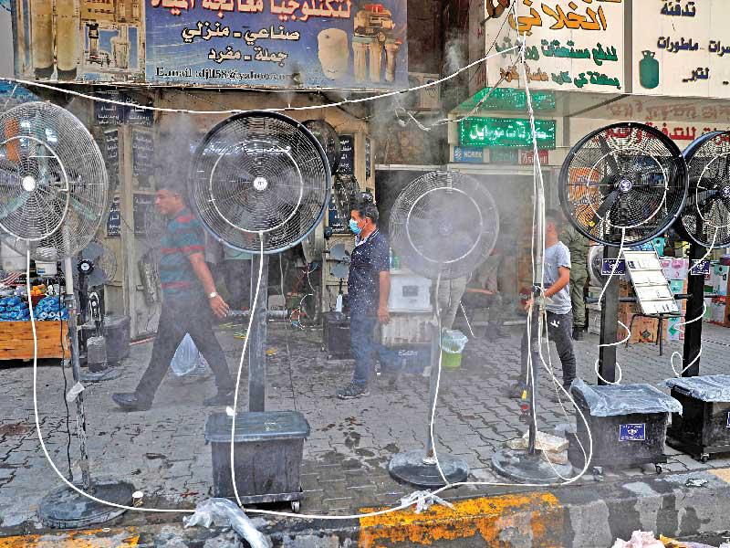عراقيون يمرون أمام مراوح ترش الماء لمواجهة موجة الحر                   (أ ف ب)   