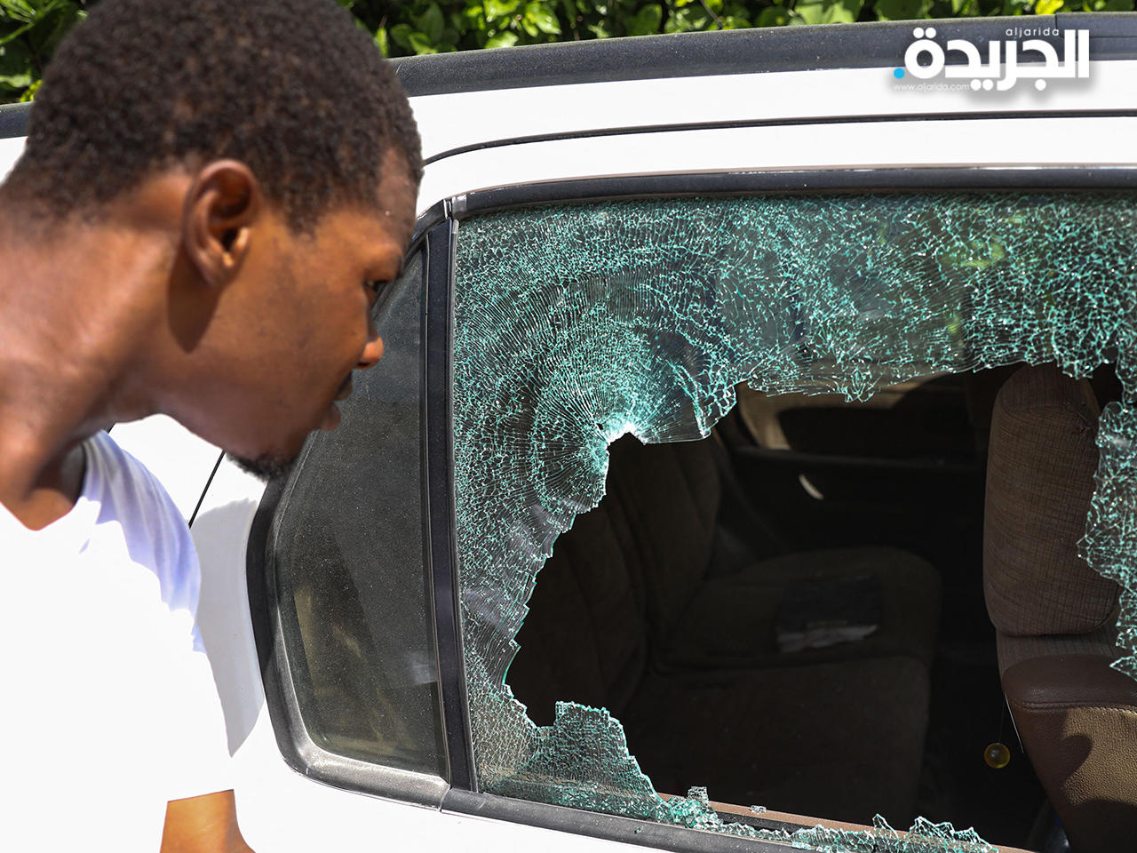 رجل ينظر إلى ثقوب الرصاص في سيارة خارج المقر الرئاسي في بورت أو برنس