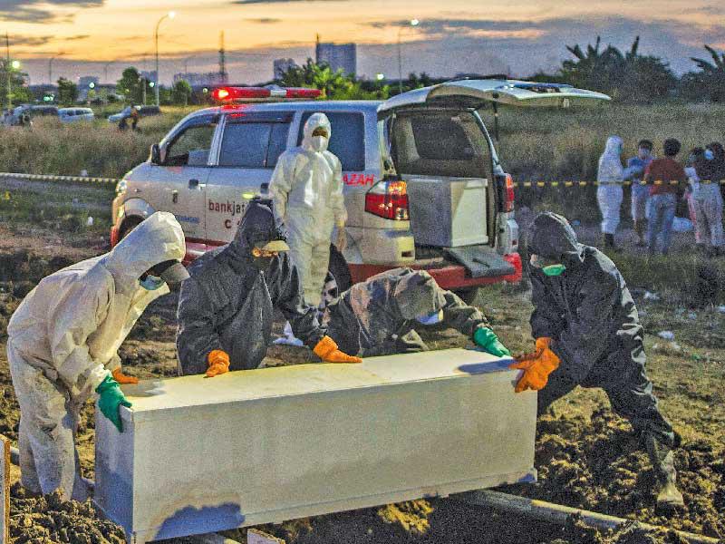 عمال مدفن في مقبرة خاصة بضحايا «كورونا» في مدينة سورابايا الإندونيسية (ا ف ب)