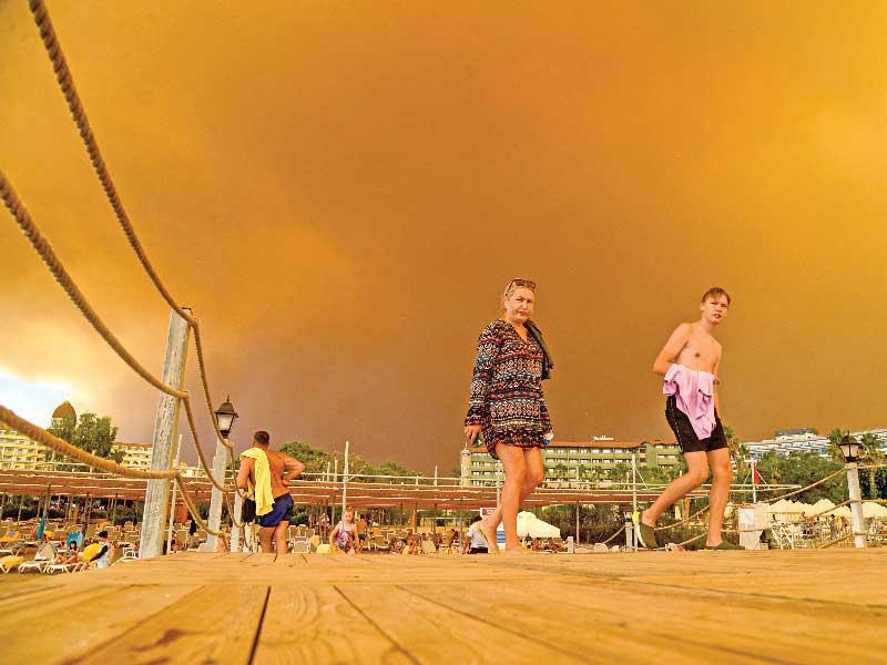  سائحان يغادران فندقهما الذي تقترب منه الحرائق في منطقة مانافغات للعطلات الشهيرة بأنطاليا (أ ف ب)