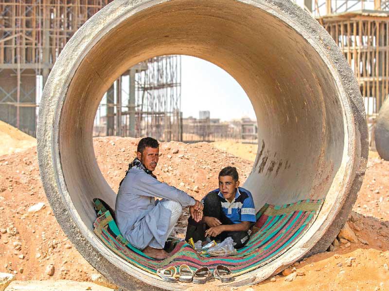 عاملان مصريان يحتميان من الشمس داخل أنبوب بمشروع العاصمة الإدارية أمس (أ ف ب)