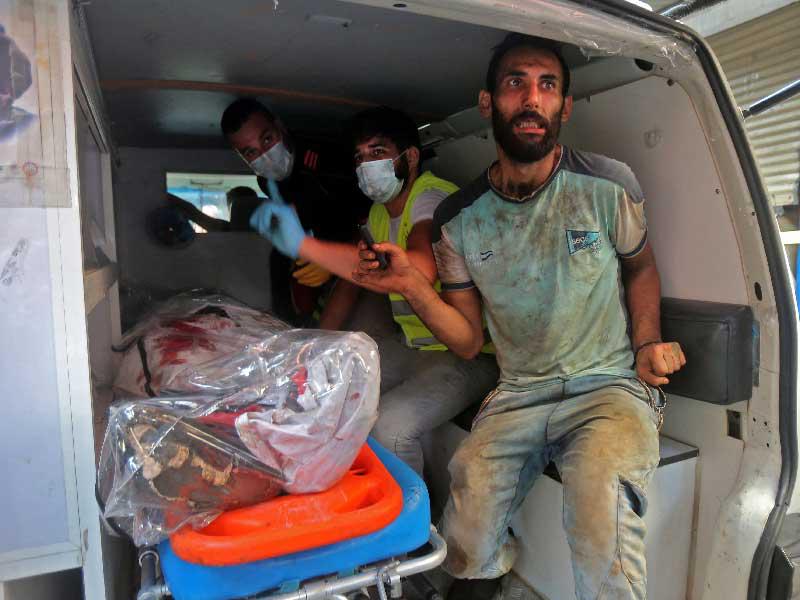 مسعفون ينقلون جريحاً وجثة ضحية من موقع انفجار مصنع في منطقة برج البراجنة