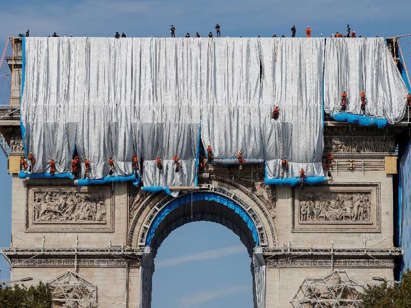 عمّال يغلّفون «قوس النصر» بشارع الشانزليزيه في باريس في الذكرى السنوية الأولى لوفاة المهندس المعماري الشهير كريستو بناء على وصيته (رويترز) 