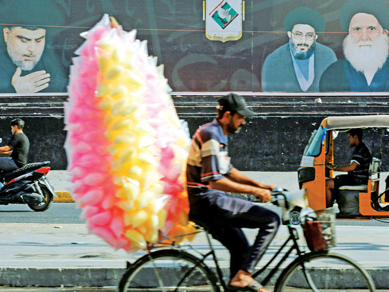 بائع متجوّل يمر أمام لافتة عملاقة للصدر في بغداد أمس (رويترز)