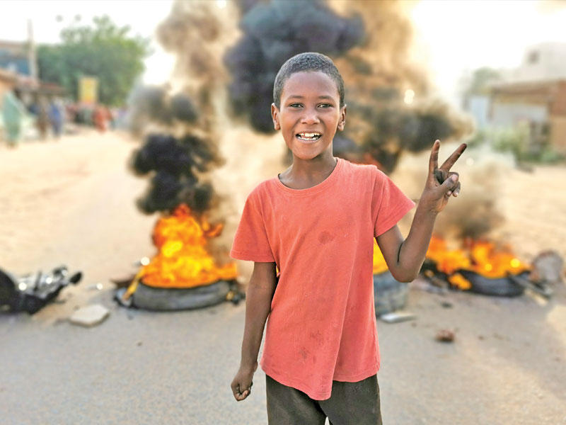 فتى سوداني أمام إطارات محروقة وضعها متظاهرون معارضون لإجراءات الجيش في الخرطوم أمس (رويترز)