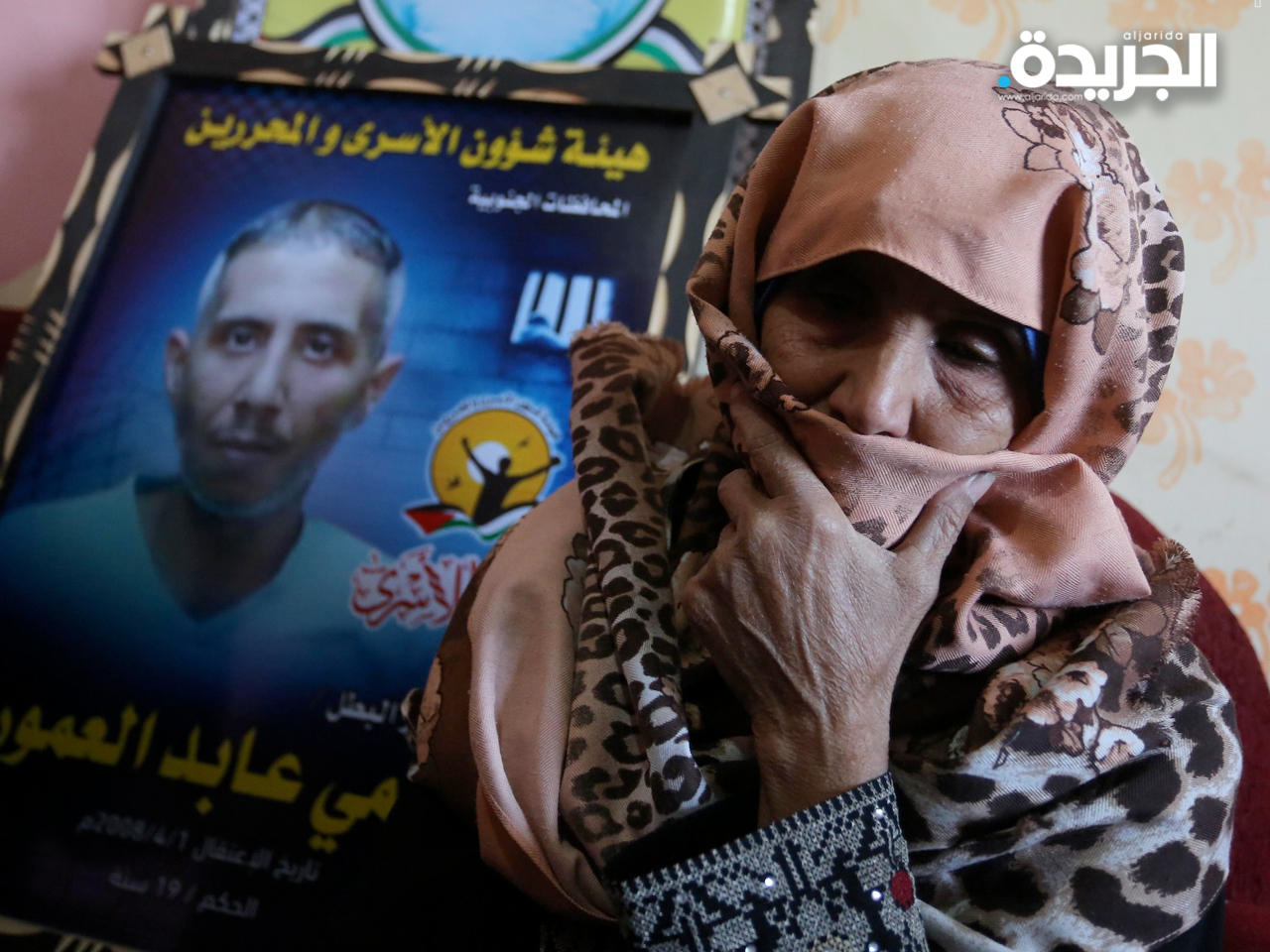 والدة الشهيد العمور.. وخلفها صورة لابنها