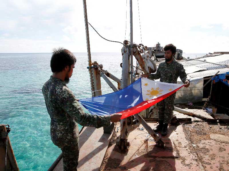  جنديان فلبينيان يطويان علم بلادهما خلال وجود سفينتهما في مياه «سيكوند توماس»         (رويترز)