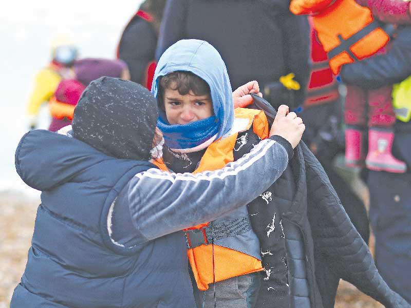 مهاجر غير شرعي يساعد طفلاً في منطقة دوغينيس البريطانية بعد عبوره «المانش» وآخرين  (رويترز)