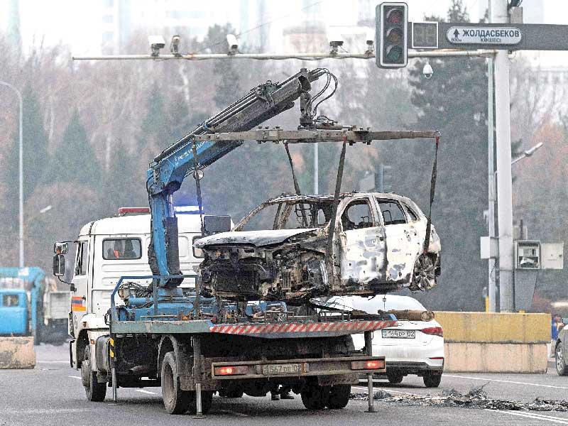 شاحنة تنقل سيارة محروقة في ألماتي أمس (رويترز)