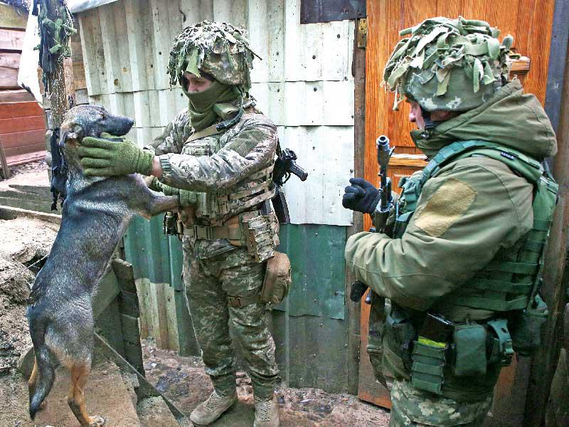 جنديان أوكرانيان يلهوان مع كلب في خندق على الجبهة الأمامية مع الانفصاليين الموالين لموسكو شرق أوكرانيا  (أ ف ب)