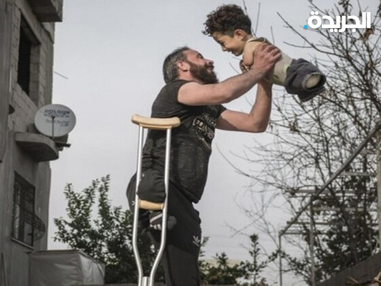 الأب السوري منذر النزال برجل واحدة ضاحكاً يحمل ابنه مصطفى 