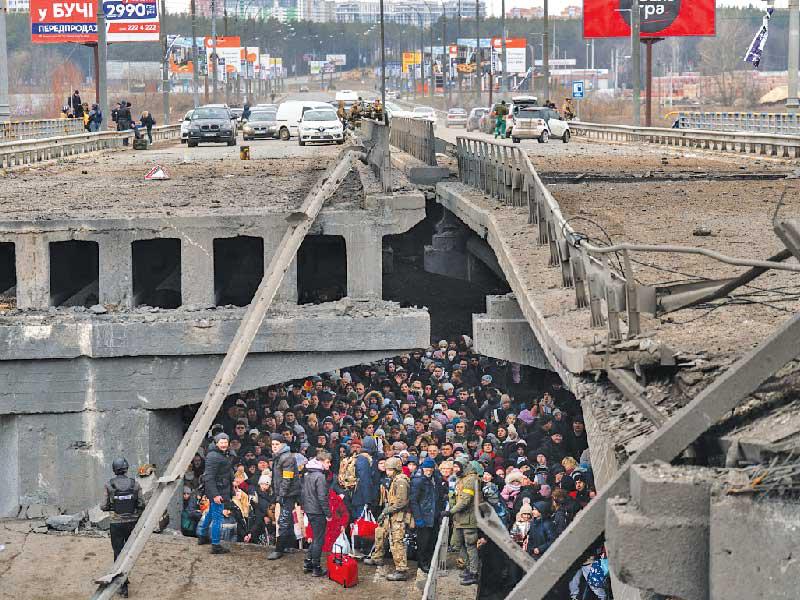  أوكرانيون يعبرون طريقًا تحت جسر دمرته غارة جوية روسية أثناء فرارهم من ضاحية إربين 