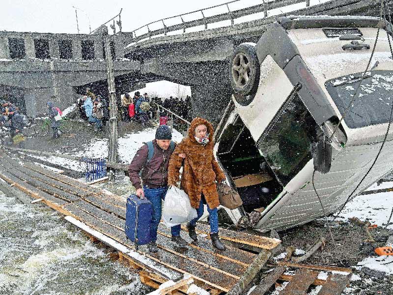 مدنيان أوكرانيان يستفيدان من وقف النار الروسي ويعبران تحت جسر مدمرٍ في مدينة إربين أمس               (أ ف ب)