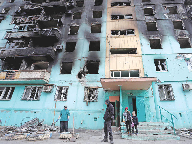 مدنيون أوكرانيون يزرعون زهور التوليب أمام مبنى محترق في ماريوبول (رويترز)