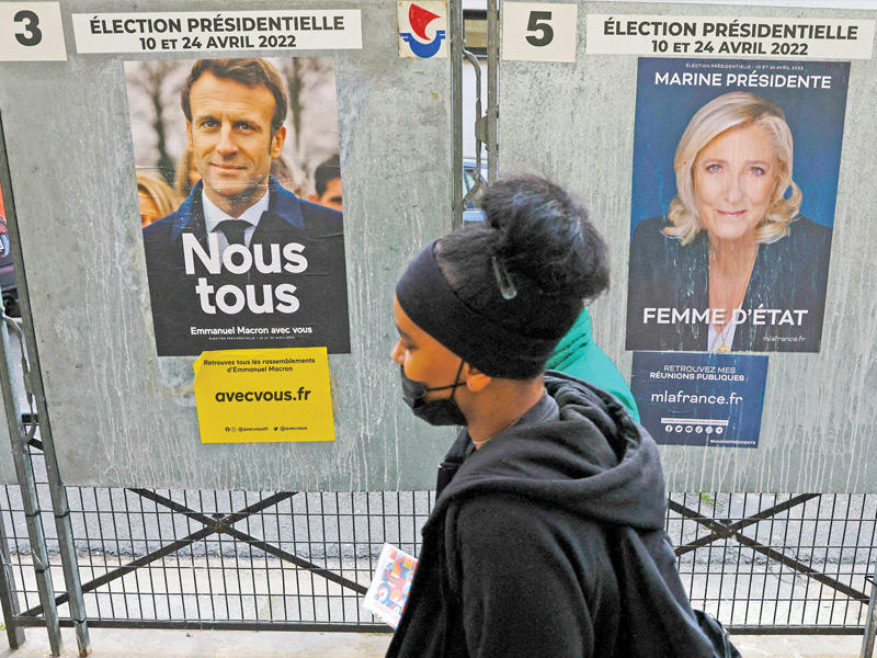 فرنسية تمر امام صورتين لماكرون ولوبن في باريس (رويترز)