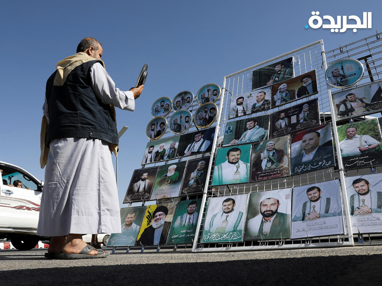 رجل يقف بجوار كشك يبيع ملصقات وصور لقادة الحوثيين في صنعاء