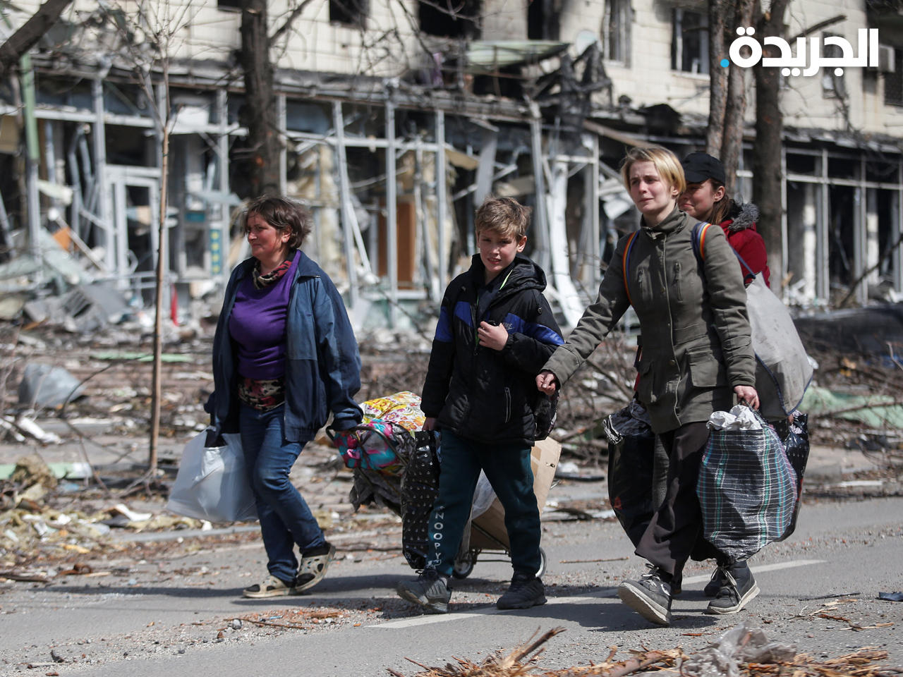 سكان يحملون أمتعتهم بالقرب من مبنى محترق في مدينة ماريوبول الساحلية الجنوبية