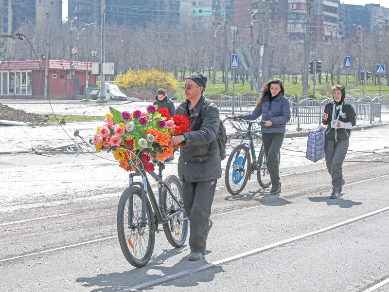 رجل ينقل باقة من الورد الاصطناعي لوضعها على قبر في مدينة ماريوبول (رويترز)