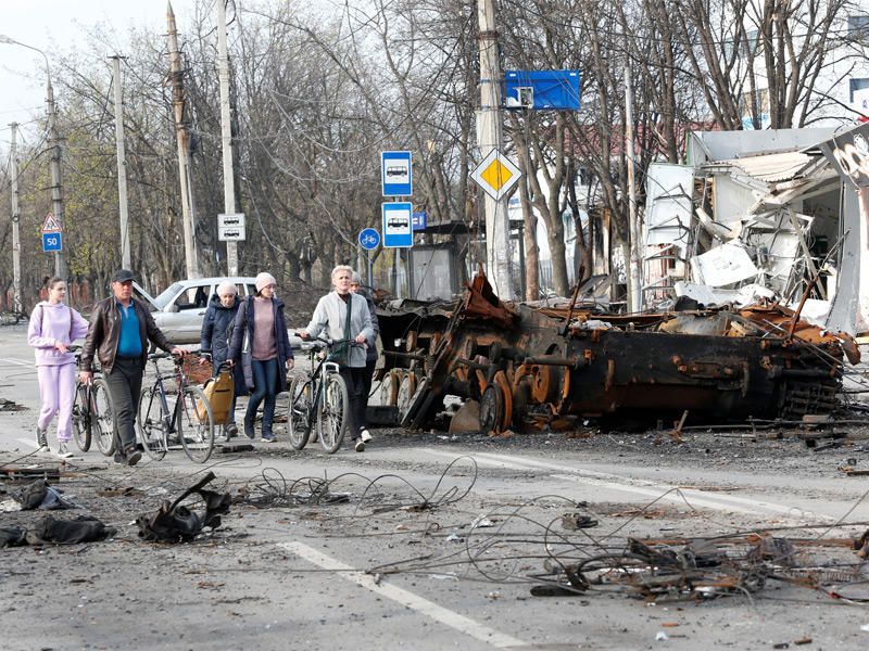 مدنيون أوكرانيون يمرّون قرب آلية عسكرية مدمّرة في ماريوبول (رويترز)