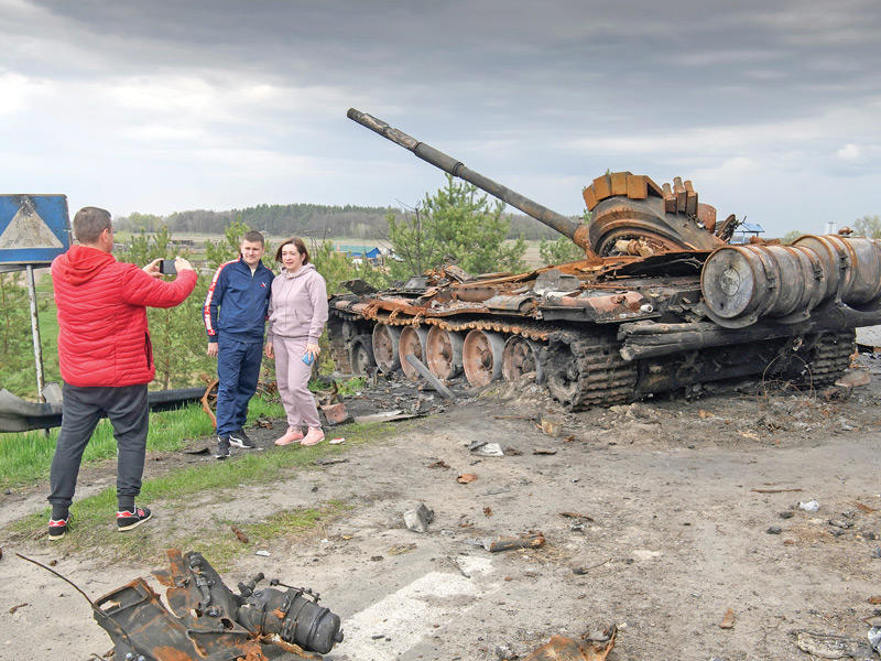 شاب وفتاة يلتقطان صورة لهما قرب دبابة روسية مدمّرة في قرية روسانيف في كييف (رويترز)
