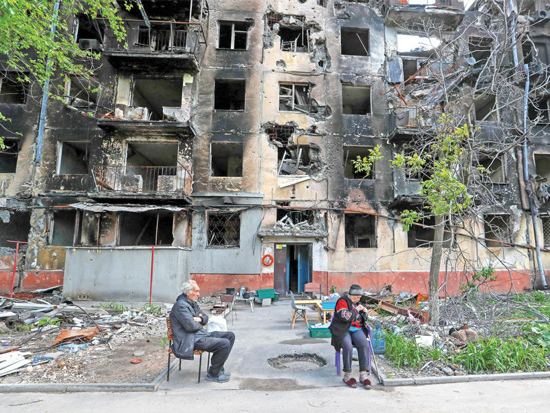 مدنيان أوكرانيان يستريحان قرب أبنية مدمّرة في مدينة ماريوبول (رويترز)  