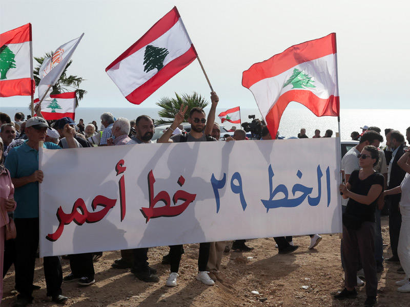 لبنانيون يحملون لافتة وأعلامًا خلال وقفة احتجاجية على استخراج إسرائيل للغاز من حقل بحري يقع في المياه المتنازع عليها قرب الحدود اللبنانية الإسرائيلية جنوب لبنان (رويترز)