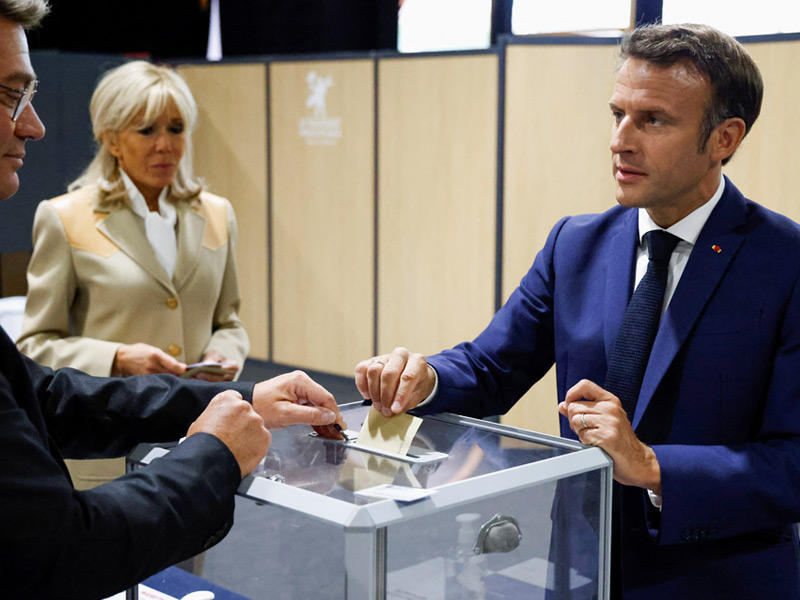 الرئيس إيمانويل ماكرون يدلي بصوته وإلى جانبه زوجته بريجيت في منطقة لو توكيه (رويترز)