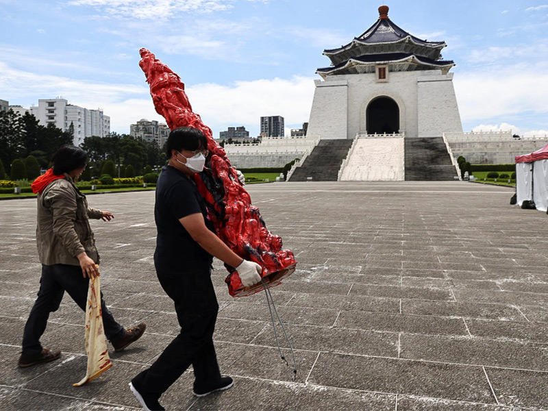موظفان ينقلان «عمود العار» الذي تم تشويهه بطلاء أسود أمام قاعة شيانغ كاي شيك التذكارية في تايبيه (رويترز)