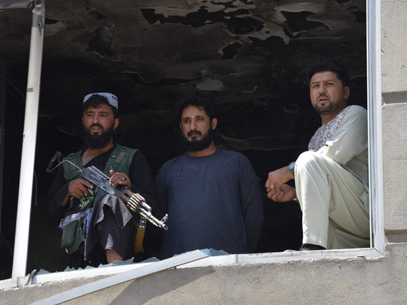 مقاتل من طالبان (يسار) ينظر من نافذة مدمرة أثناء وقوفه حارسًا في أعقاب هجوم مسلح على معبد للسيخ في كابول في 18 يونيو 2022