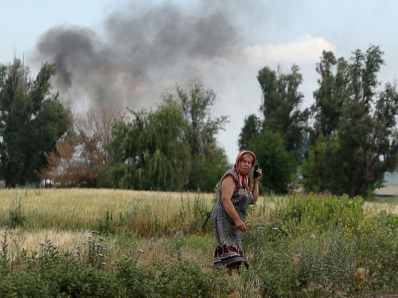 عجوز أوكرانية تتلقى اتصالاً بينما يتصاعد دخان القصف من قرية في دونيتسك (أ ف ب)