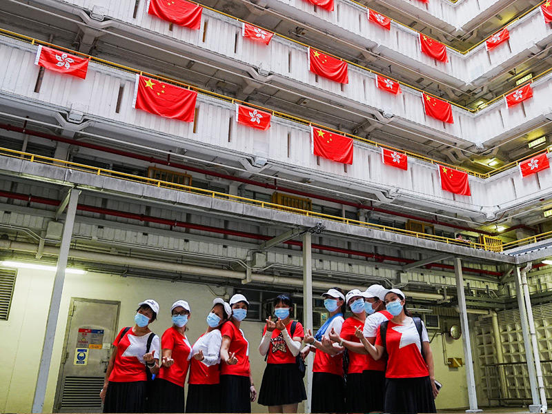 فتيات يلتقطن صوراً أمام مبنى في هونغ كونغ عُلِّقت عليه أعلام صينية مع اقتراب الاحتفال باستعادة الجزيرة من بريطانيا (رويترز)