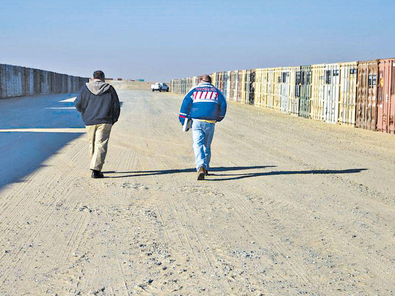 شخصان يمران بين صفوف من الحاويات في معسكر عريفجان بالكويت