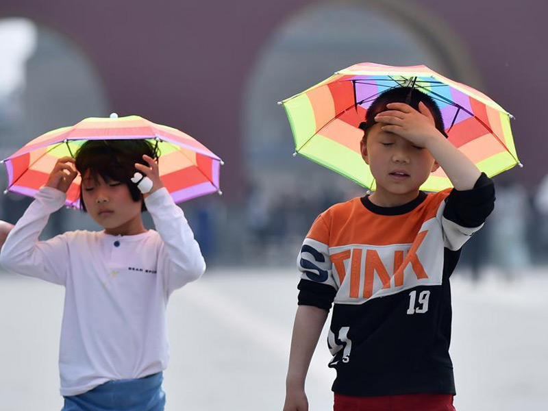 اطفال صينيون يضعون على رؤسهم شمسيات لحجب اشعة الشمس