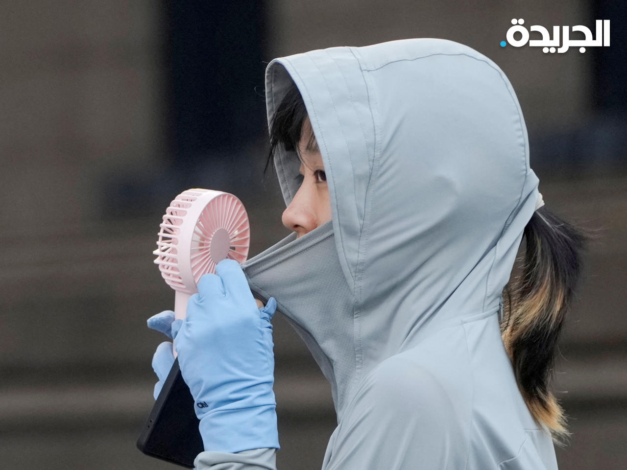 امرأة تستخدم مروحة وهي ترتدي قطعة قماش تحميها من أشعة الشمس في شنغهاي، الصين