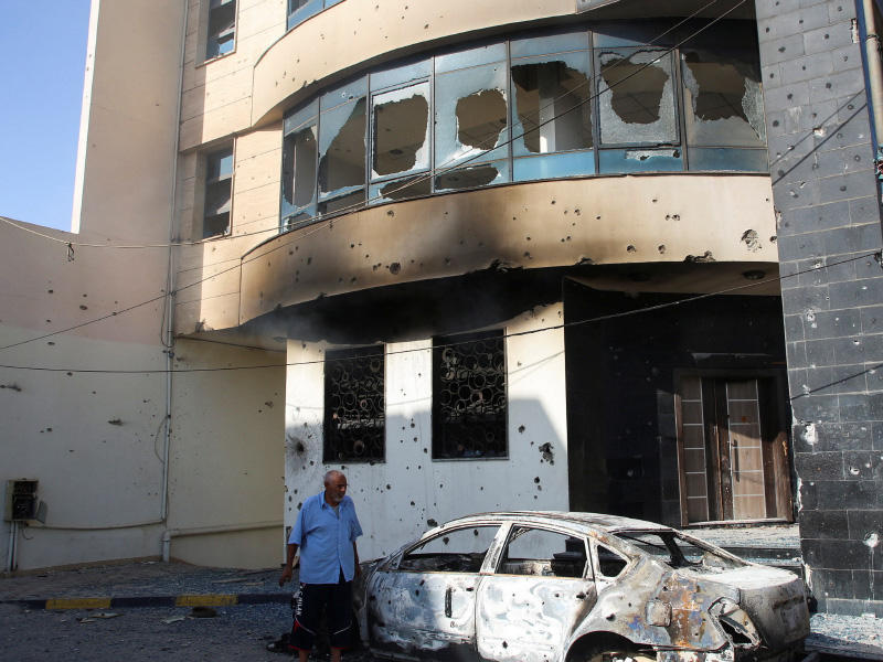 ليبي يتفقد سيارة محترقة أمام منزل مدمر في طرابلس  (رويترز)