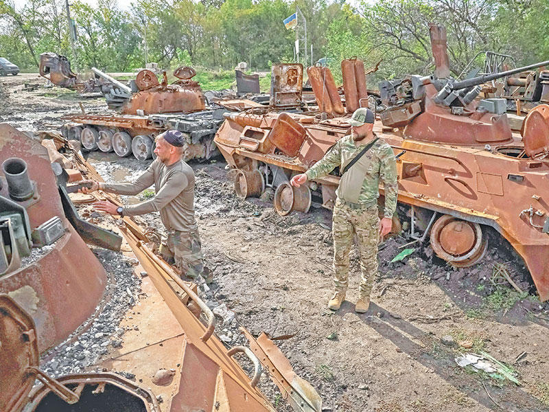 جنديان أوكرانيان وسط آليات عسكرية روسية دمرت في المعارك (رويترز)